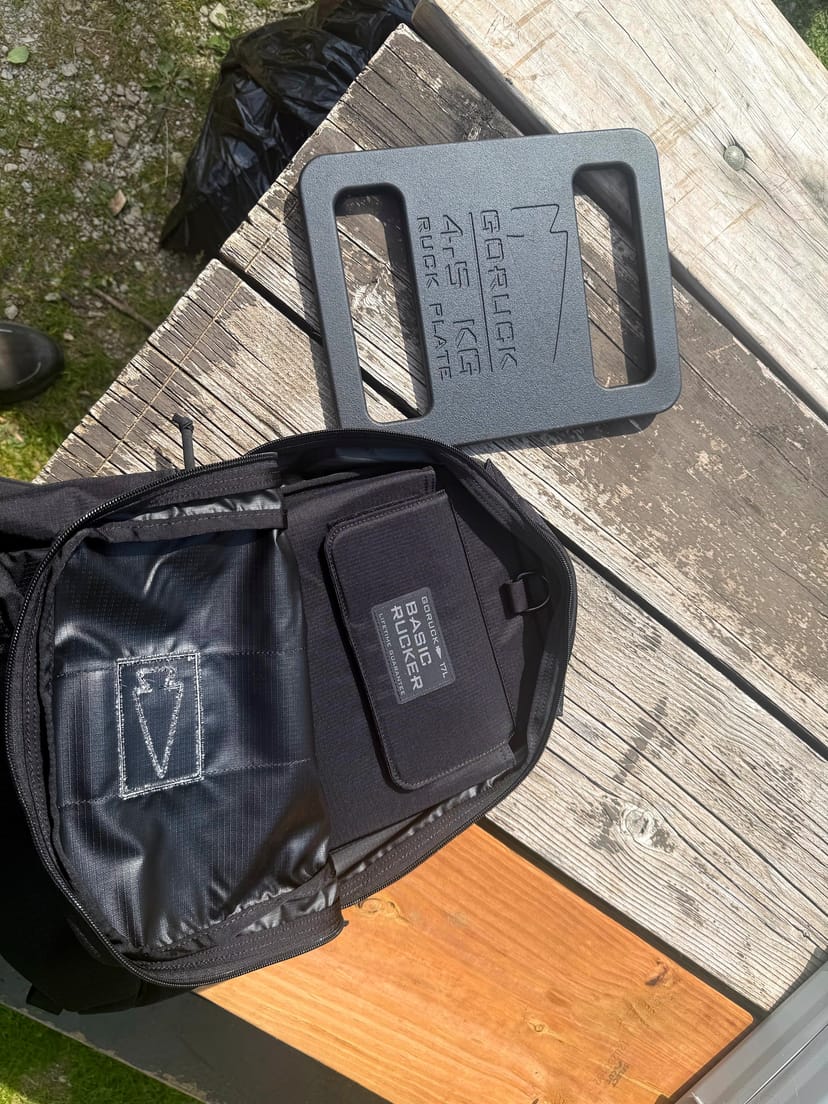 GORUCK Basic Rucker zeigt den 'Basic Rucker'-Aufnäher auf dem Rückenpanel neben einer 4,5-kg-GORUCK Ruck Plate - Detail der Plattenfach-Geometrie