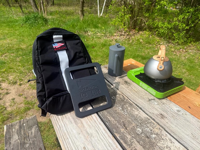 GORUCK Basic Rucker beladen mit einer 4,5-kg-Ruck-Platte, aufgestellt mit Stanley-Kaffeebereiter, Campingkocher und Kessel auf einem verwitterten Picknicktisch im Kohler-Andrae State Park
