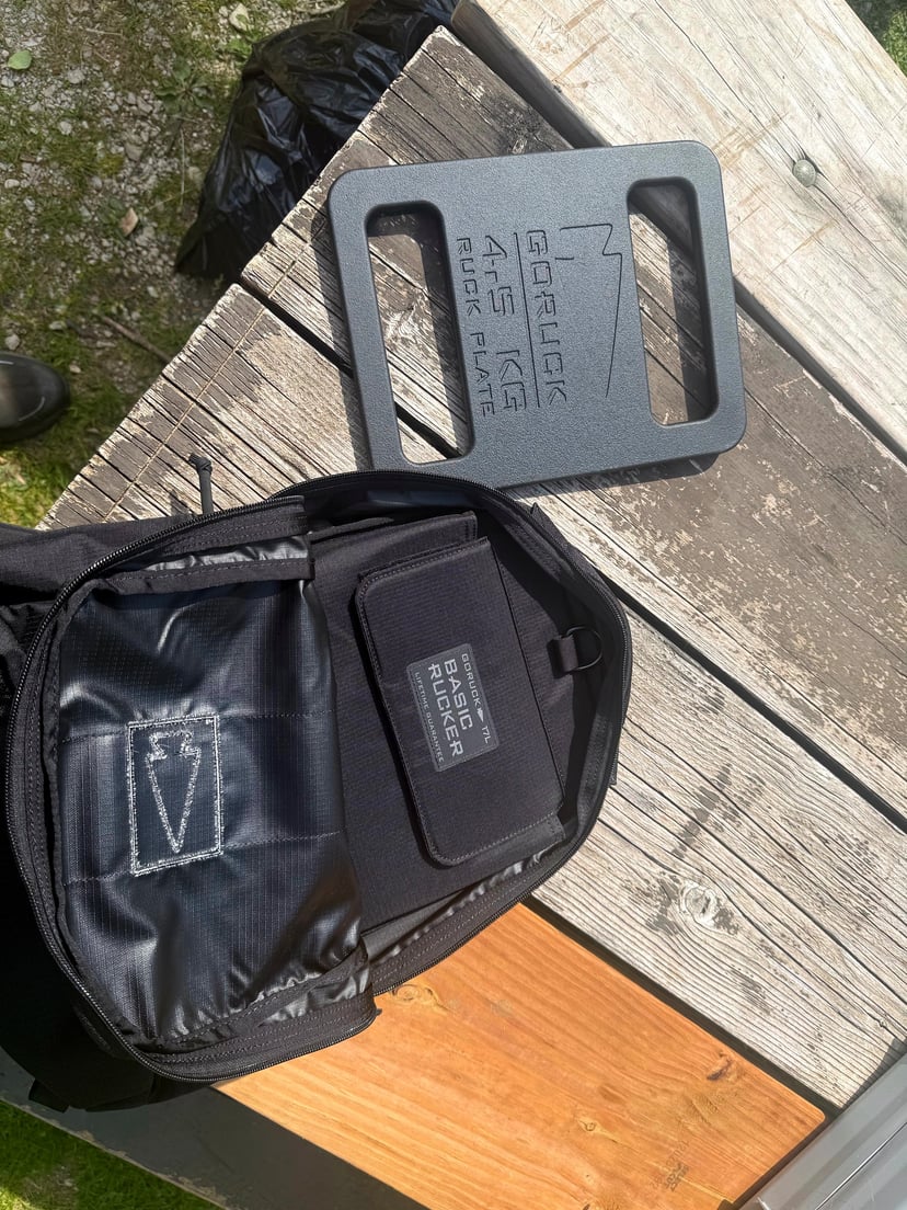 GORUCK Basic Rucker showing the 'Basic Rucker' patch on the back panel next to a 10 lb GORUCK Ruck Plate - detail of the plate-pocket geometry