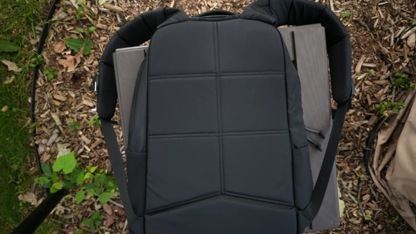 Back panel and shoulder straps of the Basic Rucker resting on wood chips, showing the padded panel with no hip belt