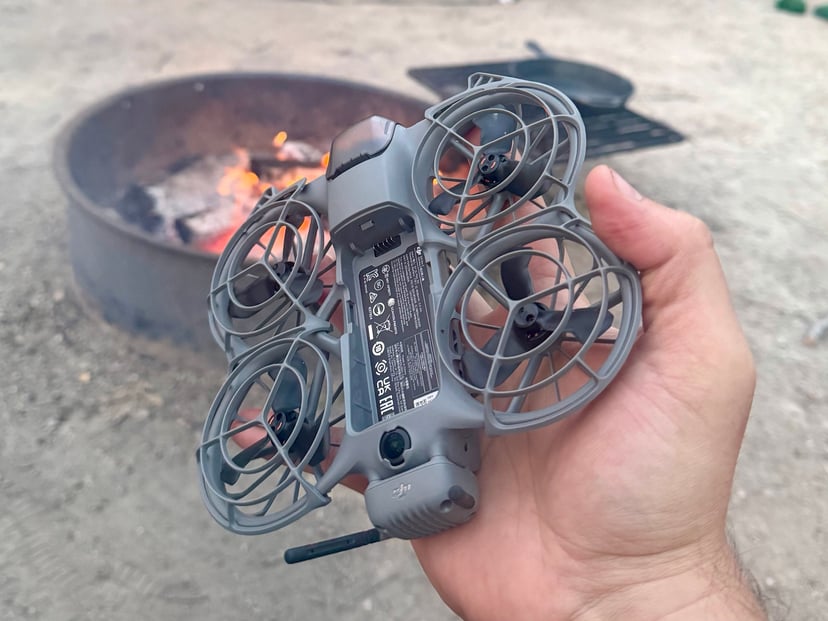 DJI Neo 2 held in hand with a glowing campfire in the background at dusk