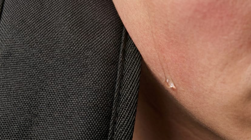 Tight macro close-up of a single sweat bead tracing skin beside the dense weave of a dark rucksack strap pressing into a shoulder - sustained physiological load without showing a full body