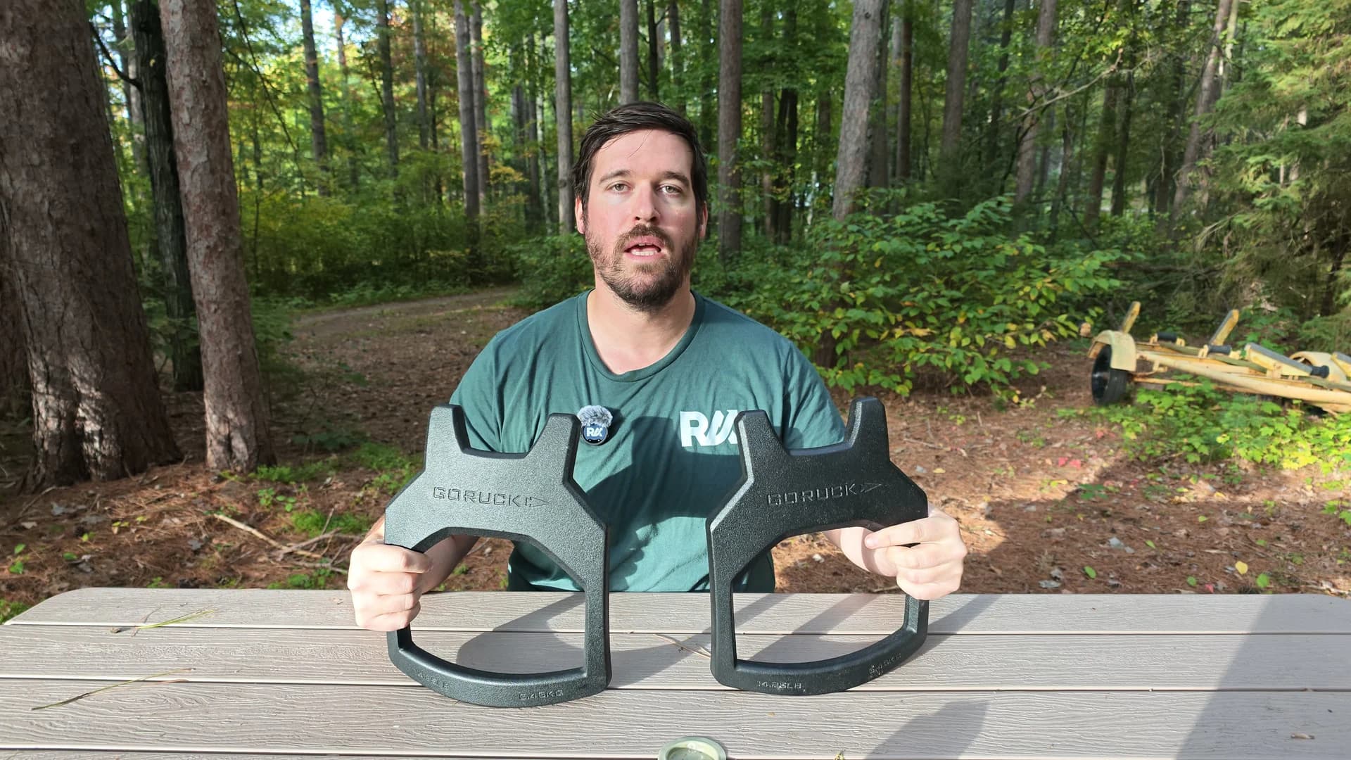Me holding two different GORUCK Curved plate weight options at a picnic table